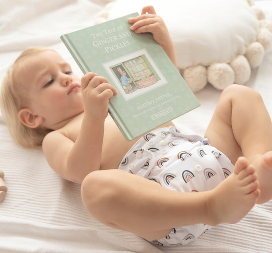 baby is holding a book while wearing baby elsa diaper cover