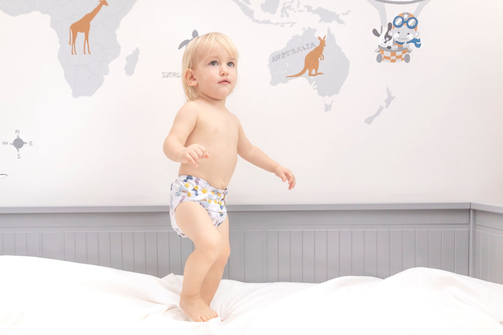 a boy is standing on a bed in baby elsa cloth diapers