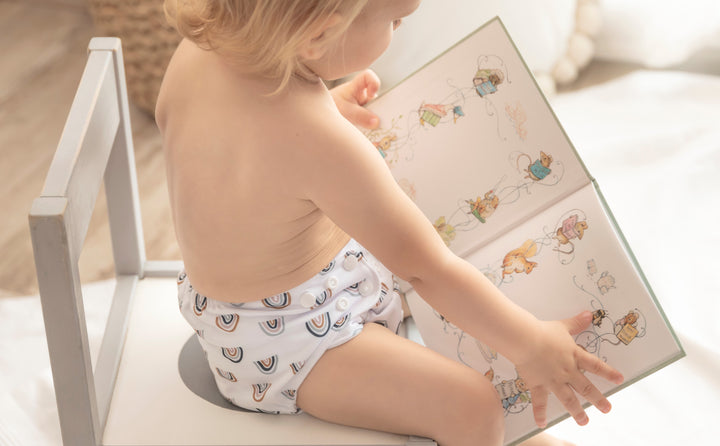 Boy sitting and reading a book while wearing a Baby Elsa cloth diaper Rainbow pattern
